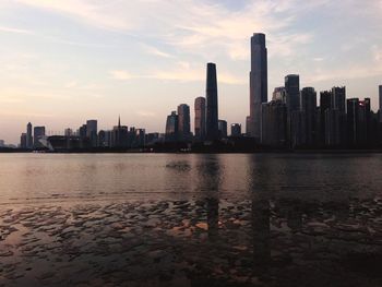 Sea by cityscape against sky during sunset