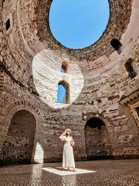 Woman standing inside ancient roman building with natural light shining on her.