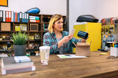 Young woman using mobile phone while sitting on table