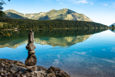 Stacked stones pyramide like zen on the lake shore and mirroring of mountains on the blue water 