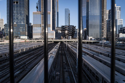 High angle view of trains against modern buildings in city seen through railing