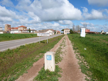 Milestone by information sign on roadside against cloudy sky
