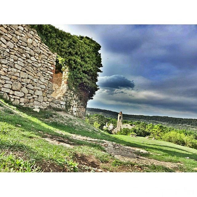 built structure, architecture, sky, building exterior, grass, landscape, field, green color, stone wall, cloud - sky, tranquility, house, tranquil scene, nature, tree, hill, cloud, old ruin, day, old