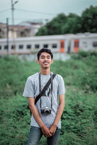 Portrait of young man with camera standing on field