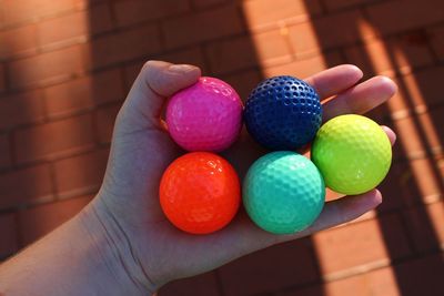 Cropped hand of woman holding colorful golf balls over floor