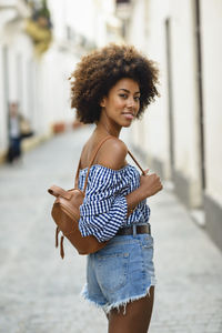 Portrait of fashionable young woman with small backpack on the street