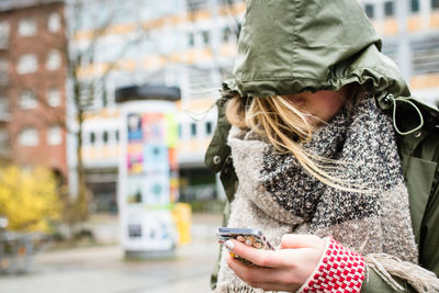 Close-up of woman in raincoat using mobile phone on street