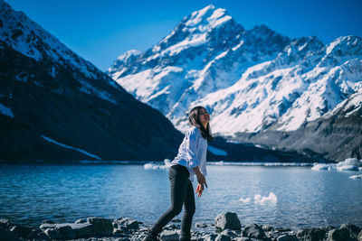 Woman standing on snowcapped mountain by lake against sky