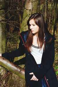 Beautiful young woman standing by tree trunk in forest