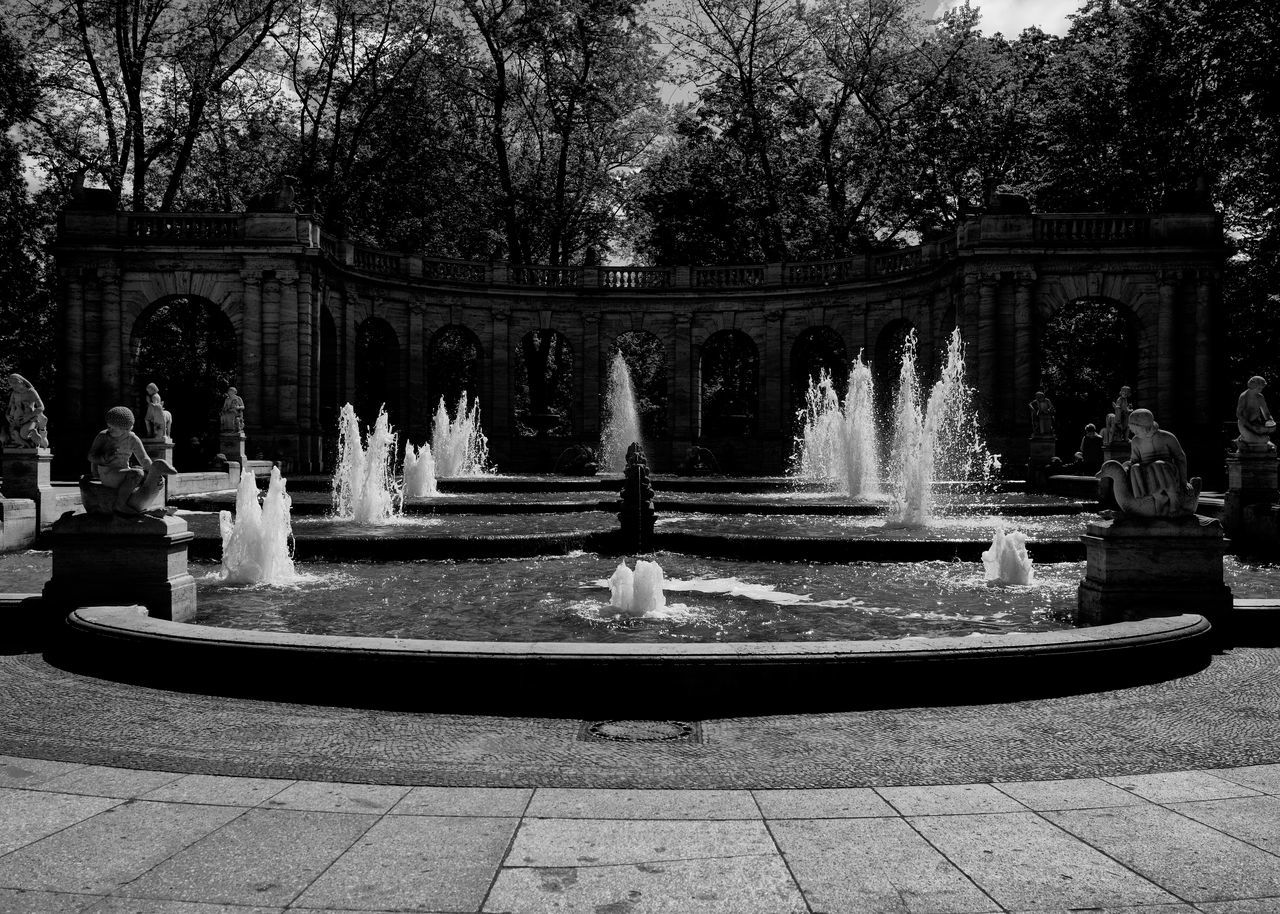 tree, fountain, plant, architecture, nature, water feature, built structure, black and white, water, day, sculpture, park, monochrome photography, monochrome, no people, outdoors, statue, park - man made space, building exterior, representation, creativity, garden, the past, town square, human representation