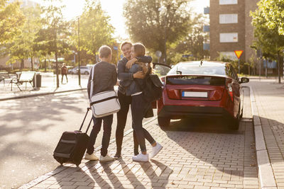 Smiling mother embracing daughter while son standing at roadside