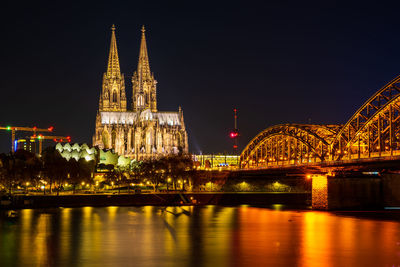 Illuminated bridge over river against buildings at night