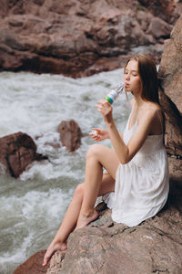 Young woman sitting on rock at shore