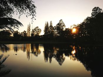 Reflection of silhouette trees in lake against sky during sunset
