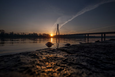 Silhouette bridge over sea against sky during sunset