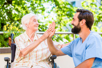 Happy nurse giving high-five to senior woman sitting on wheelchair