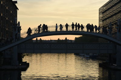 People on bridge over river in city against sky