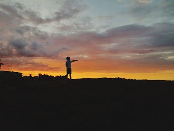 Silhouette man standing on field against sky during sunset