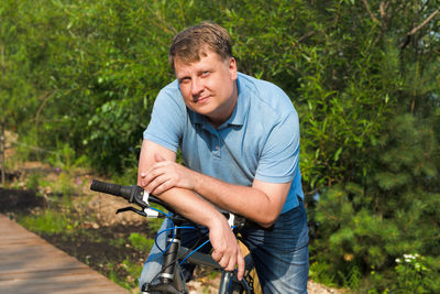 Portrait of adult male blond 40-44 years old with a wide smile sitting on a bicycle.