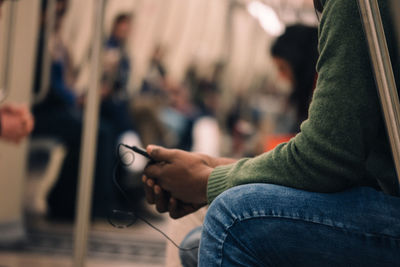 Midsection of man holding mobile phone in train