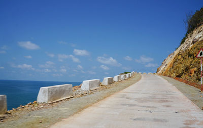Empty road at mountain by sea against blue sky