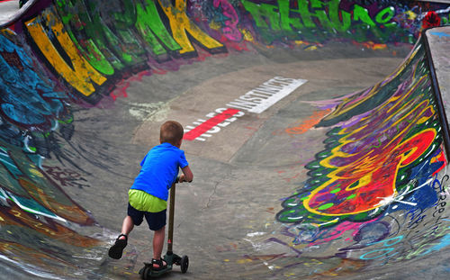 Rear view of boy riding push scooter at skateboard park