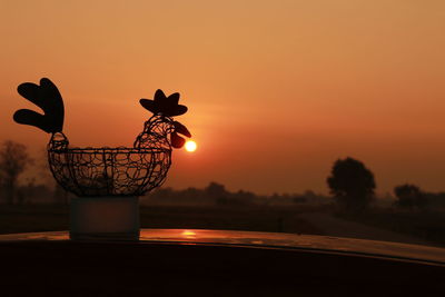 Close-up of silhouette lamp on table against orange sky