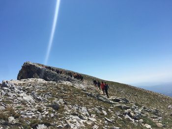 People on rock against clear blue sky