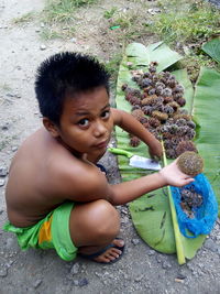 Portrait of boy holding fruit while crouching on ground