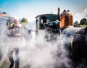 Man walking by steam train at railroad station