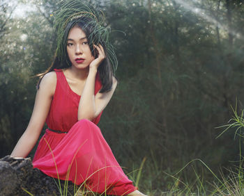 Young woman looking away while sitting on land