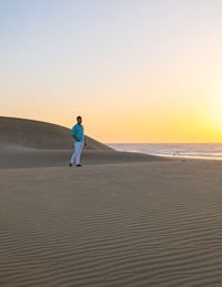 Rear view of woman walking at beach against clear sky during sunset