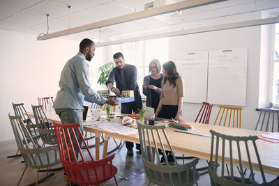 Male engineer holding architectural model while standing with colleagues at table during office meeting