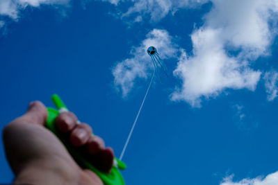 Low angle view of hand flying kite against blue sky