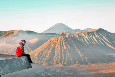 Man sitting on mountain against sky