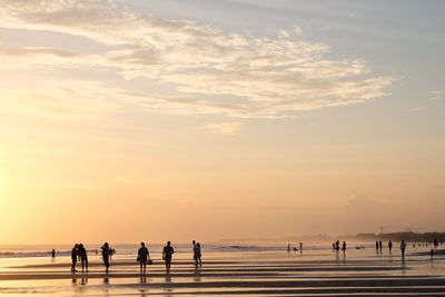 Silhouette people at beach against sky during sunset