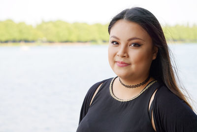 Portrait of smiling young woman against lake