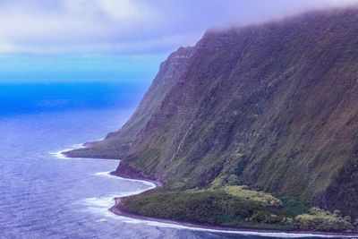 Scenic view of sea by mountain against sky