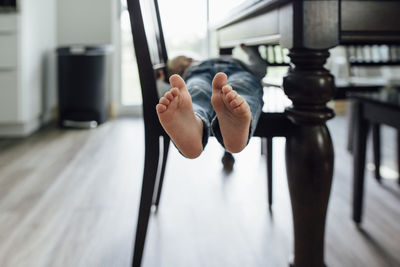 Low section of baby boy lying on chair by table at home