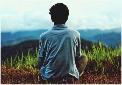 Rear view of woman sitting on field against sky