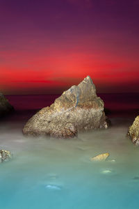 Rocks in sea against sky during sunset