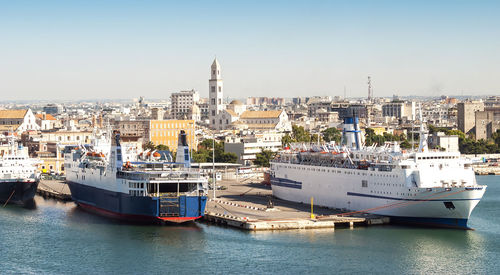 Ships moored on harbor at sea against cityscape