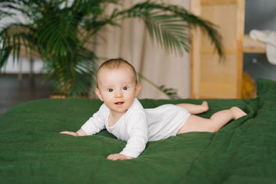 Little boy of 6 months is lying on his stomach on a bed in a cozy room, the child is smiling