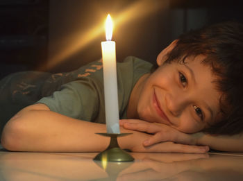Child looking at a lit candle lying on the floor of the house. 