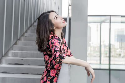 Young woman looking away while standing against wall