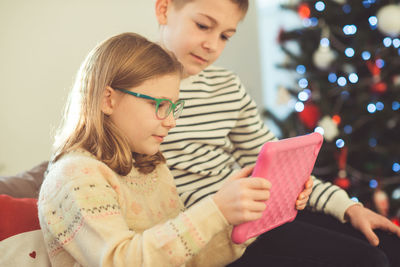 Siblings using digital tablet at home during christmas