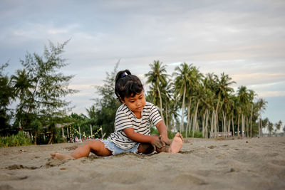 Boy sitting on sand at beach against sky