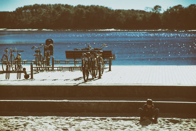 Boy playing in sand against bicycles on rack by lake