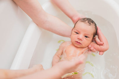 From above unrecognizable parent washing crying newborn baby in warm water in basin at home