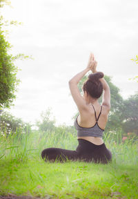 Rear view of woman practicing yoga while sitting on grassy field against clear sky